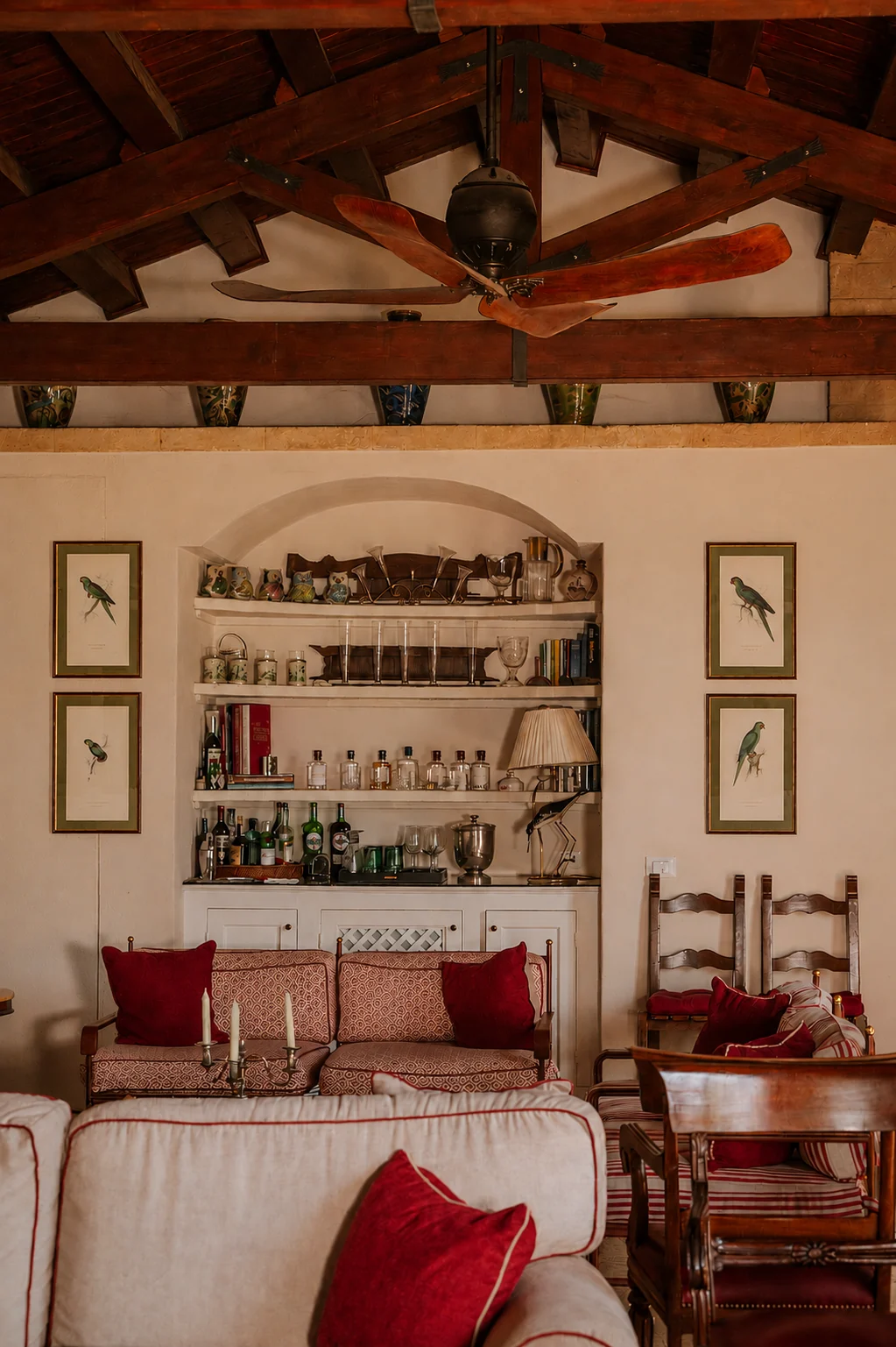 Traditional living room and bar at Aranjaya in Sicily, with exposed wooden beams, red furnishings and framed bird prints.
