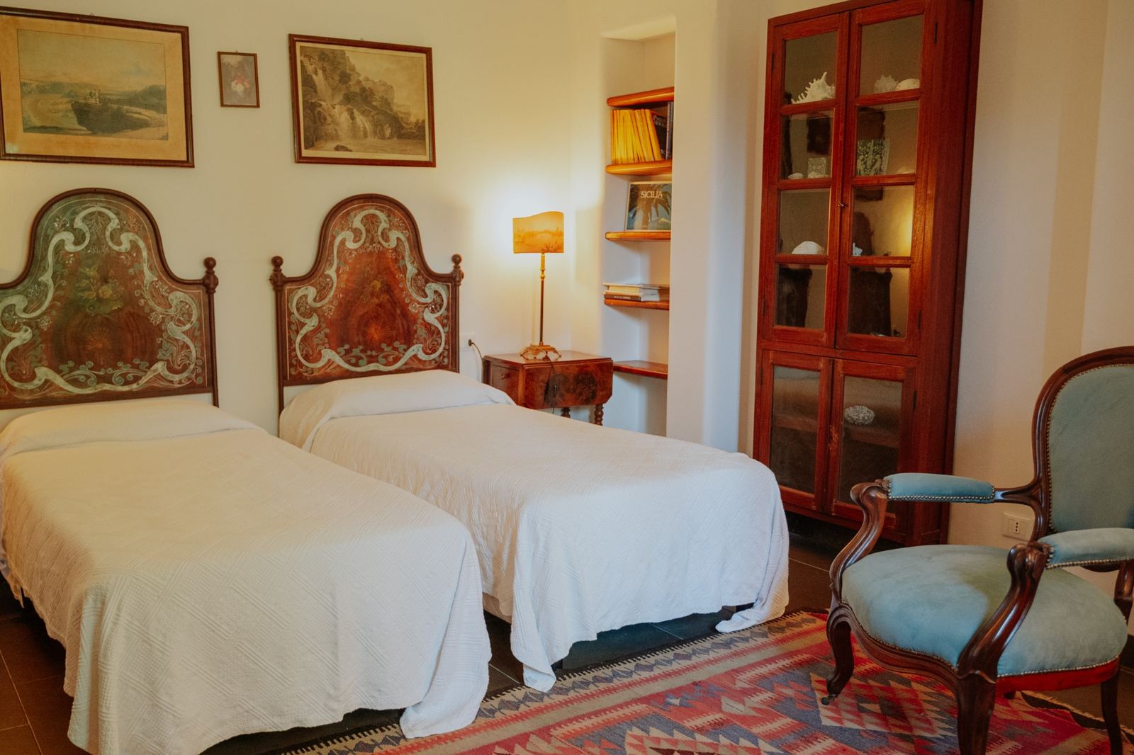 Twin bedroom at Aranjaya in Sicily with antique painted headboards, Sicilian furniture and a traditional rug.